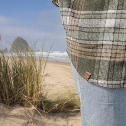 Person wearing a plaid shirt with a brand logo on a beach