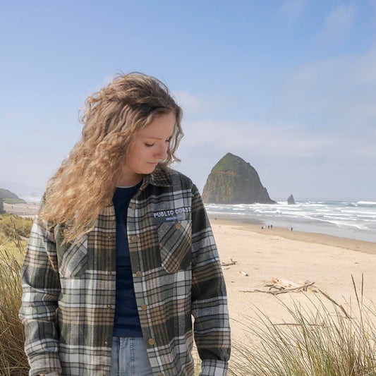 Person wearing a plaid shirt on a beach with a rock in the background